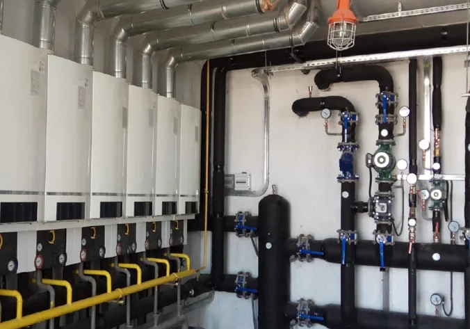 Commercial boiler room with multiple wall-mounted units, gas lines, and piping for industrial hot water and heating systems.